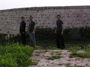 Three young men stand next to the Acco fortress wall