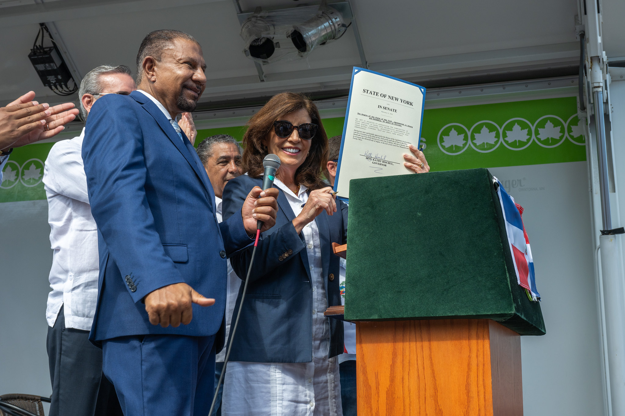 Kathy Hochul signs a bill at the Dominican Day Breakfast in the Bronx, as Deputy Speaker Phil Ramos looks on.
