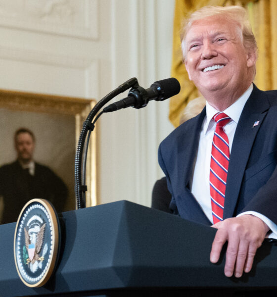 Donald Trump speaking with gold and white backdrop