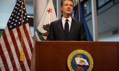 Governor Gavin Newsom (D-Calif.) at podium bearing governor's seal with USA and California flags on posts behind him.