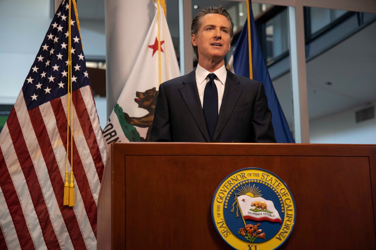 Governor Gavin Newsom (D-Calif.) at podium bearing governor's seal with USA and California flags on posts behind him.