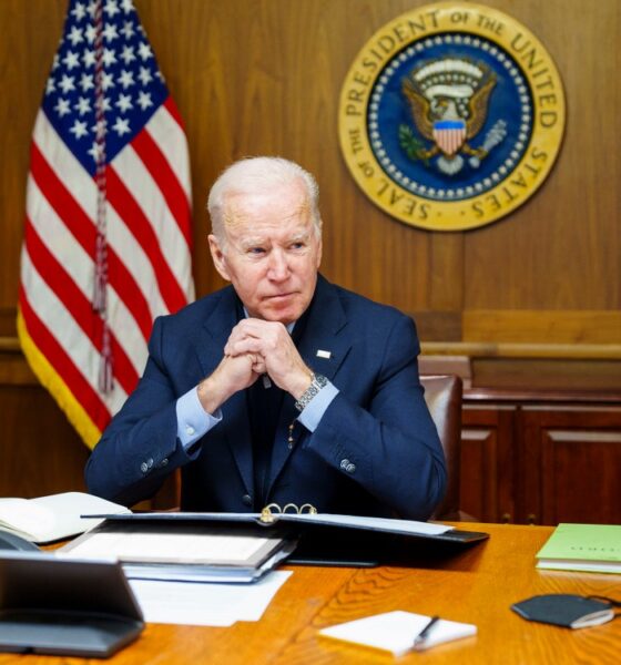 Joe Biden at desk or Cabinet Room table with paneled wall with Presidential Seal behind him.