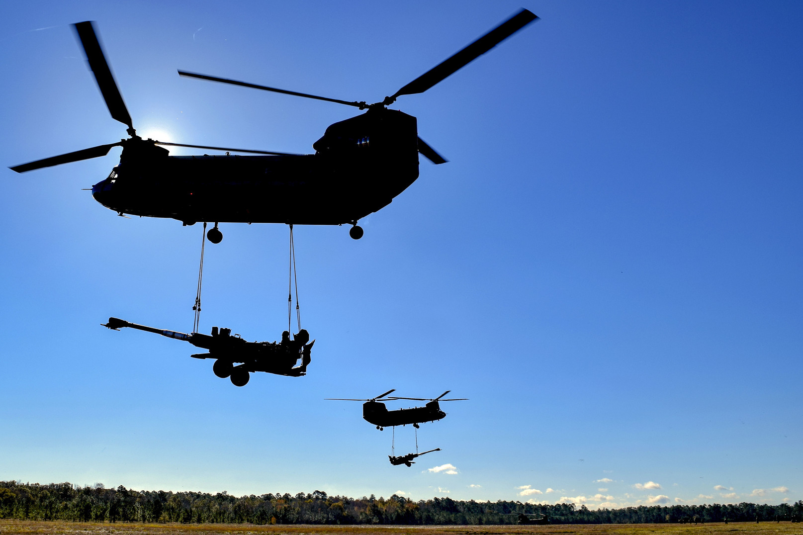Two CH-47 Chinook helicopters lift heavy artillery pieces during training at Fort Stewart, Georgia