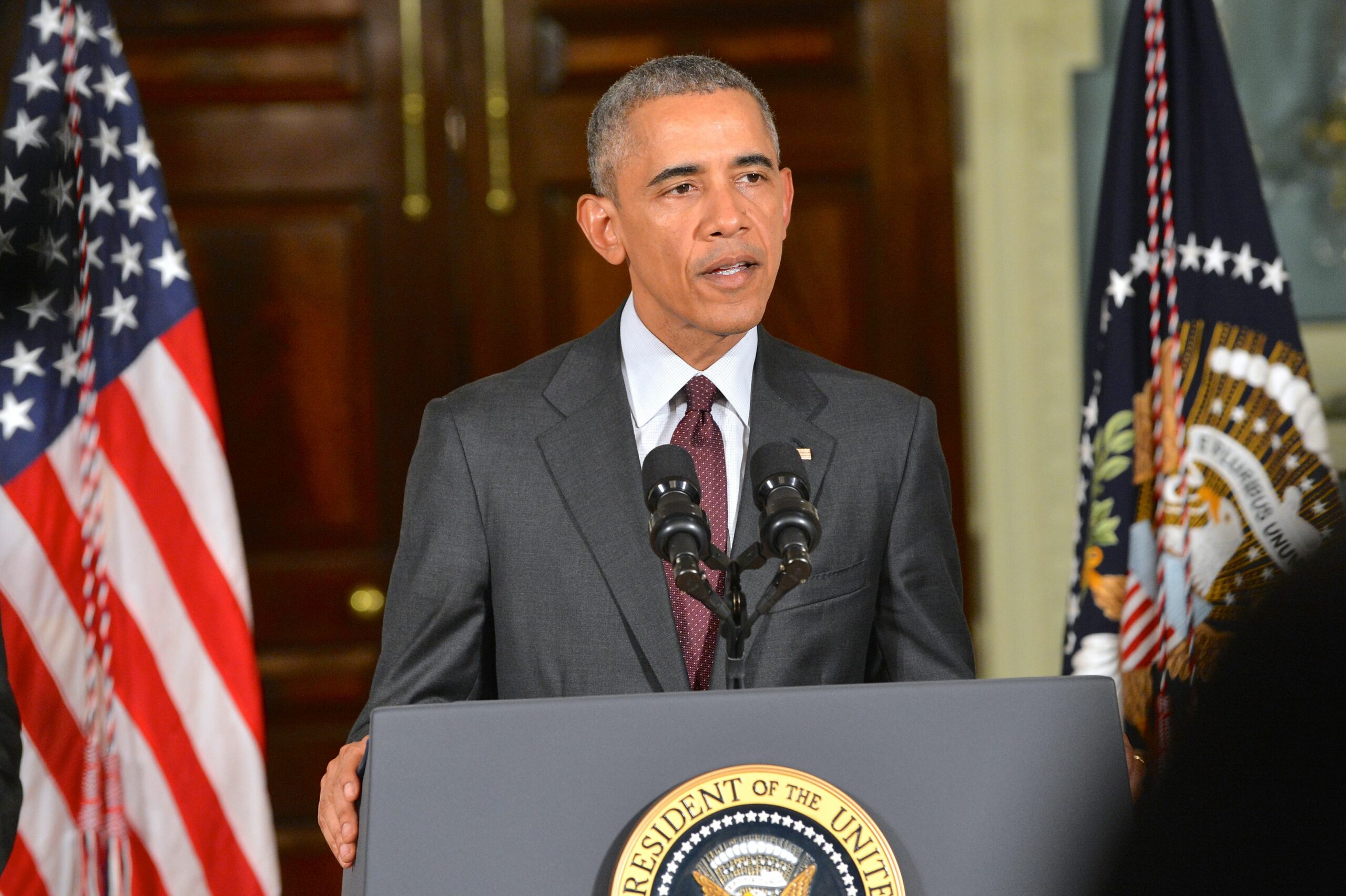 Barack Obama speaks with America and State Department flags behind and to either side