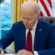 Biden front left angle in Oval Office with window behind him signing a bill