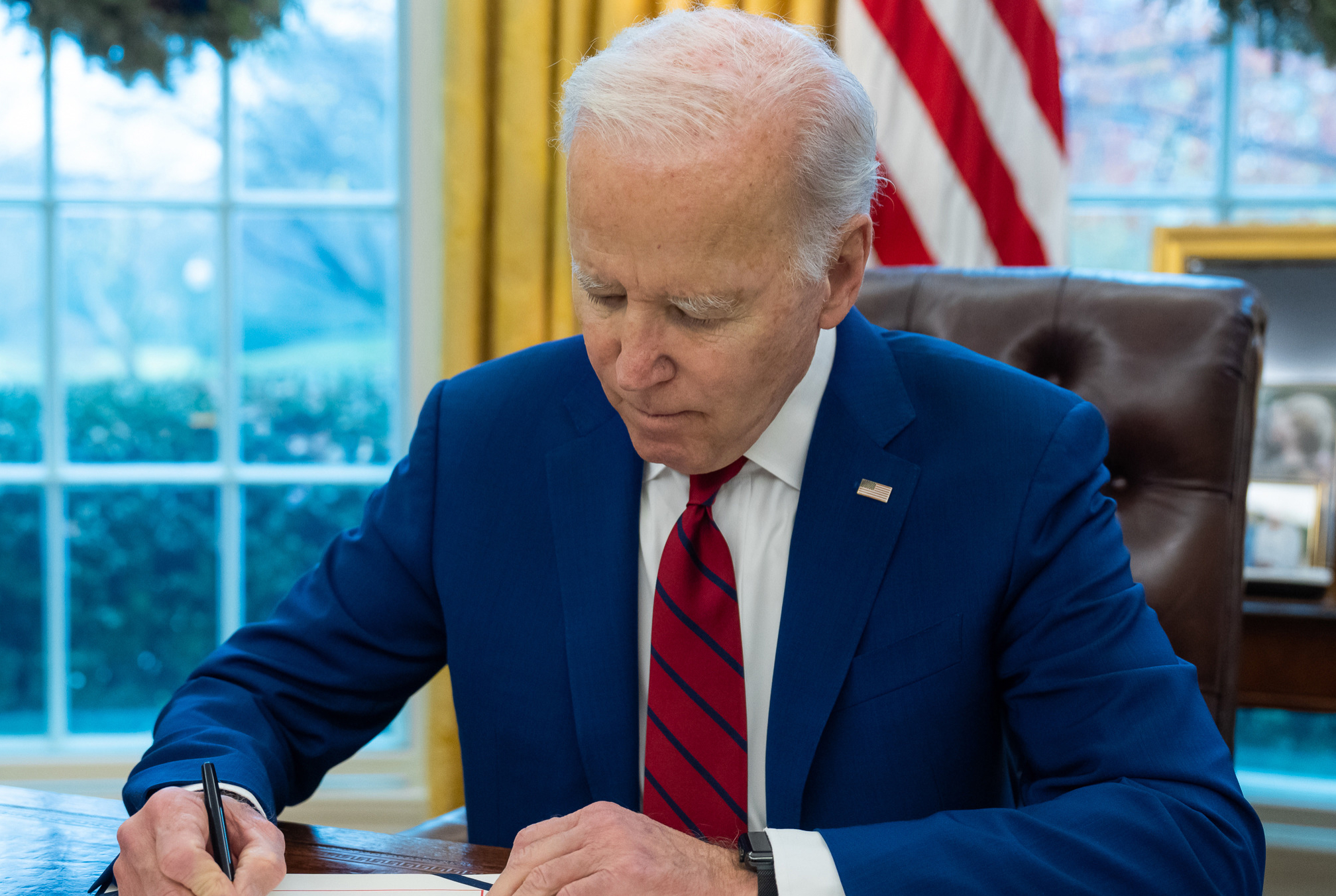 Biden front left angle in Oval Office with window behind him signing a bill