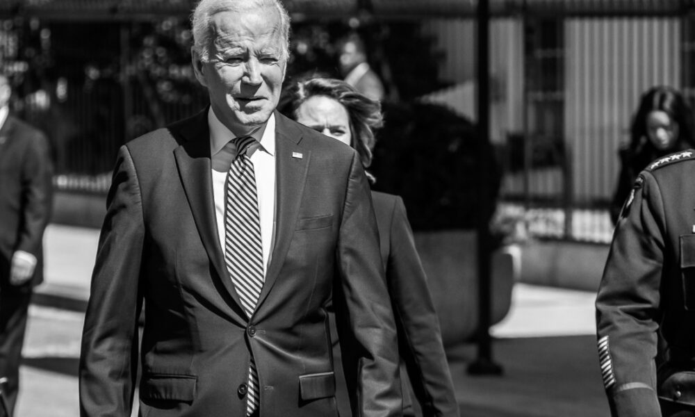 Biden in black-and-white image walking next to a general, with Vice-President Kamala Harris behind and to his left