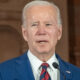 Joe Biden in front of a wall with an arch outline barely discernible behind him