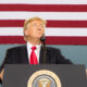 Donald Trump as President speaking with USA flag stripes behind him