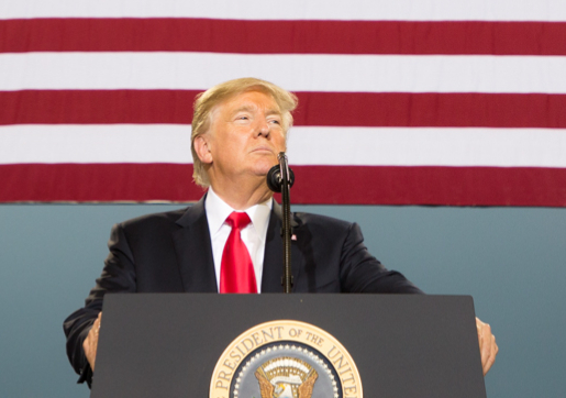 Donald Trump as President speaking with USA flag stripes behind him