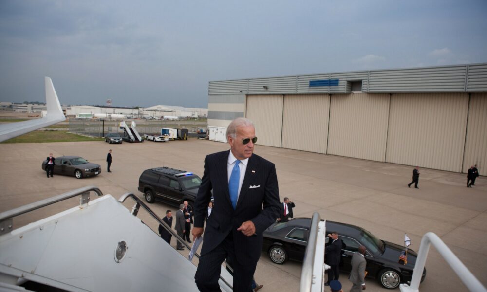 Biden boarding his aircraft - viewpoint looking out at tarmac and looking at Biden as he manages the last steps.