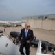 Biden boarding his aircraft - viewpoint looking out at tarmac and looking at Biden as he manages the last steps.