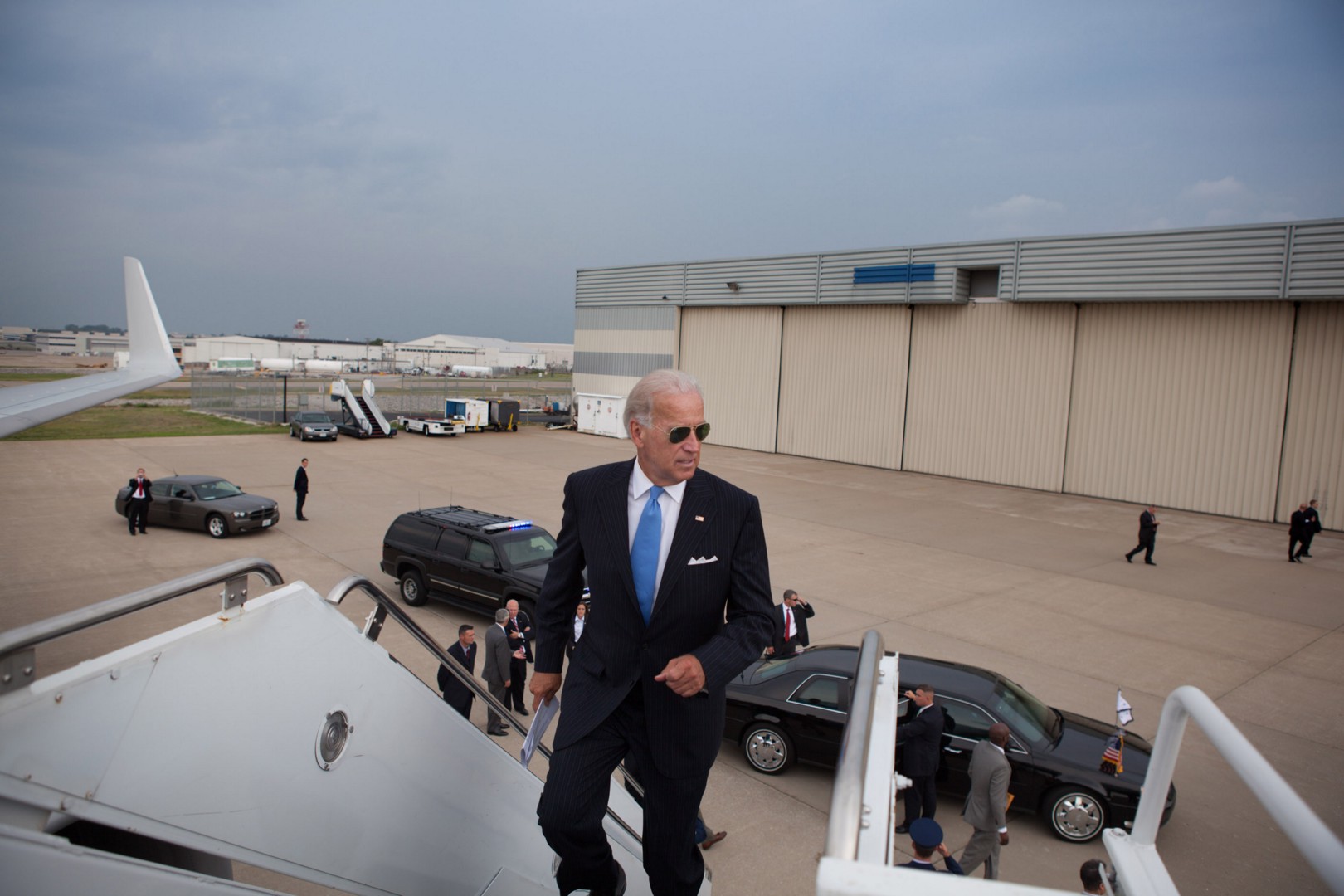 Biden boarding his aircraft - viewpoint looking out at tarmac and looking at Biden as he manages the last steps.