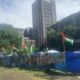 Campus protest camp with Palestine flags flying eye-level view with cityscape background