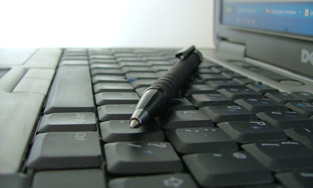 A Dell laptop computer with a pen resting on the keyboard