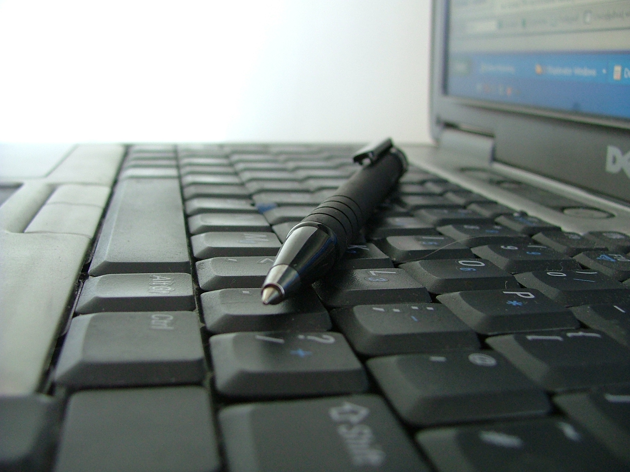 A Dell laptop computer with a pen resting on the keyboard