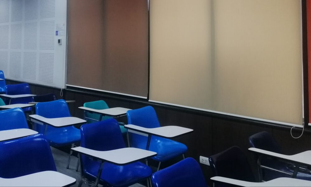 Classroom with blue chairs, multicolored marking boards, red doors, and corkboard with sheets of binary code