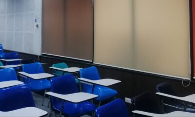 Classroom with blue chairs, multicolored marking boards, red doors, and corkboard with sheets of binary code