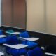 Classroom with blue chairs, multicolored marking boards, red doors, and corkboard with sheets of binary code