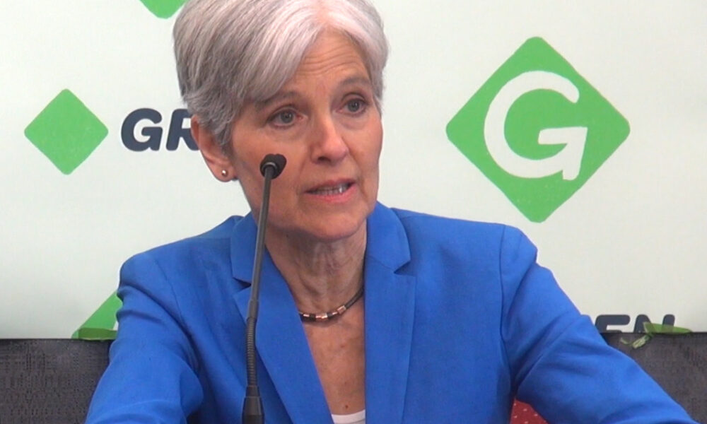 Jill Stein seated before Green Party photo-op backdrop