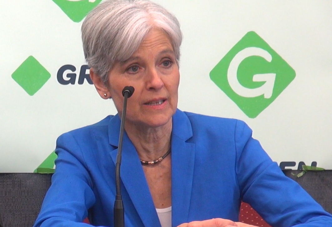 Jill Stein seated before Green Party photo-op backdrop