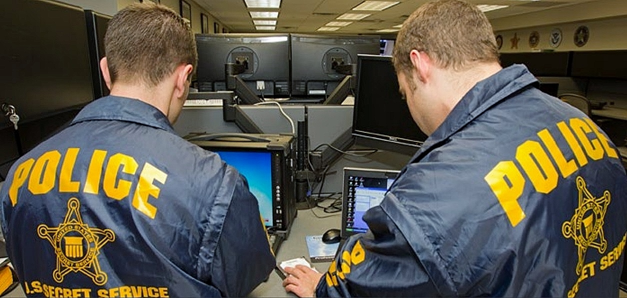 Two Secret Service agents, wearing official windbreakers, pore over computer monitors as they conduct a preliminary investigation