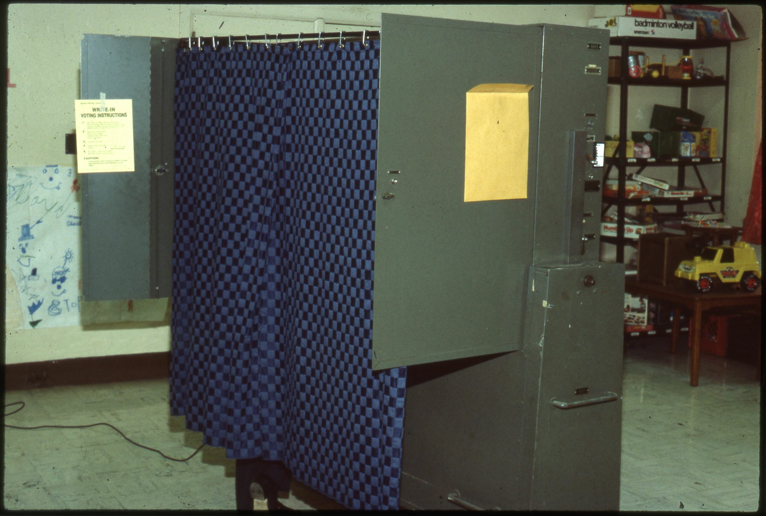 Voter voting at a Print-O-Matic mechanical lever-pull voting machine. The Officer of Election who should have pushed in the button to unlock the big red Close Curtains and Vote lever has stepped out of the shot.