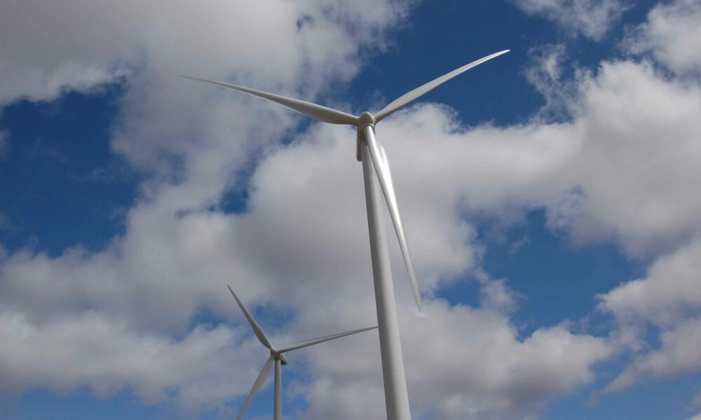 Two wind turbines in line under a partly cloudy sky