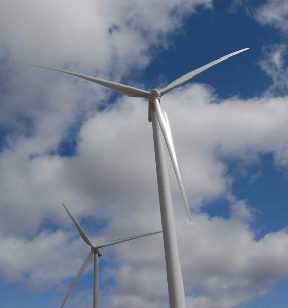 Two wind turbines in line under a partly cloudy sky