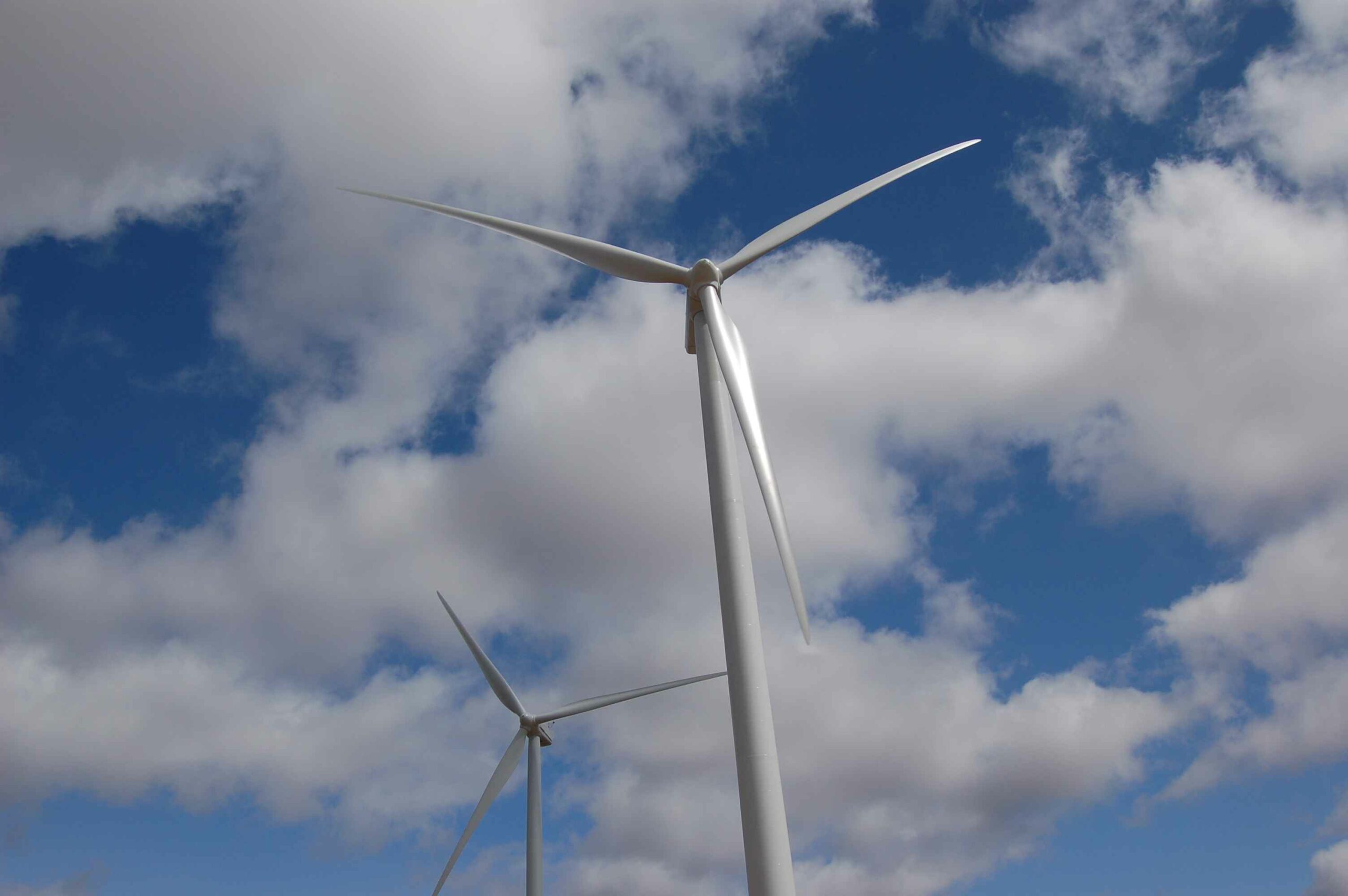 Two wind turbines in line under a partly cloudy sky