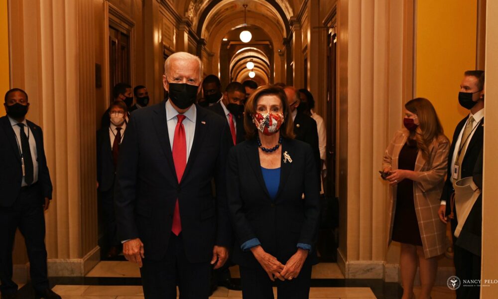 Joe Biden and Nancy Pelosi walk down a corridor - and everyone is masked up in fear of the dreaded coronavirus, putative cause of COVID