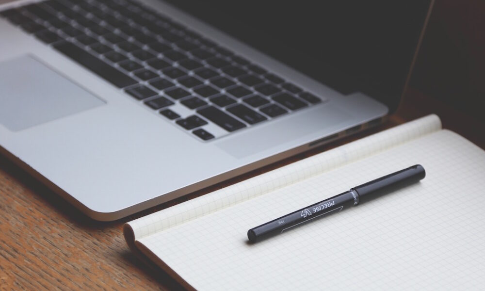 A laptop next to a notebook with gridlines and a marking pen.