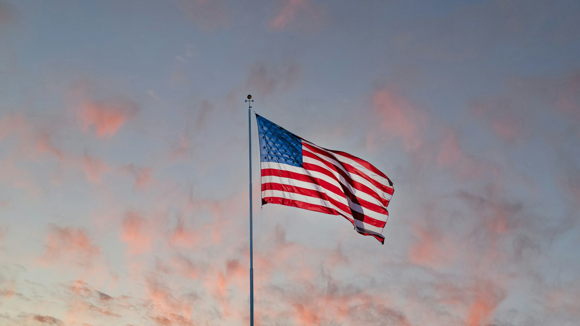 USA flag flying under partly cloudy sky at sunset