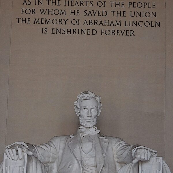 Abraham Lincoln seated in his famous chair in the Lincoln Memorial. Above him is his epitaph.