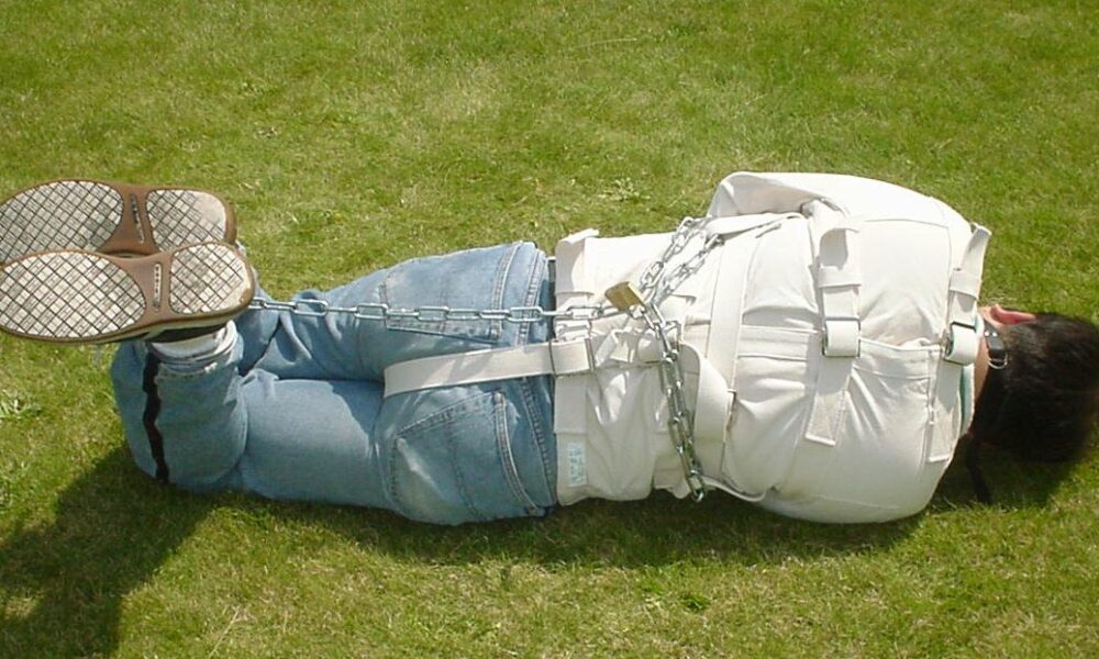 Man in a straitjacket and chains, photographed from the rear