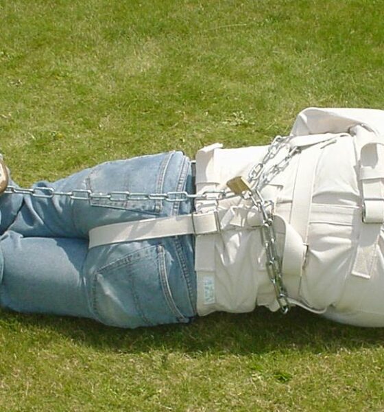 Man in a straitjacket and chains, photographed from the rear