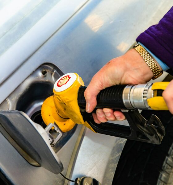 A man holds a gasoline pump nozzle. The stylized seashell, yellow with red outline, is a registered trademark of Royal Dutch Shell. Photo by Jesse Donoghue on Unsplash.com.