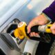 A man holds a gasoline pump nozzle. The stylized seashell, yellow with red outline, is a registered trademark of Royal Dutch Shell. Photo by Jesse Donoghue on Unsplash.com.