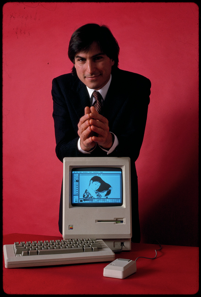 Steve Jobs, founder of Apple Computer, shown with his most famous invention, the first Apple Macintosh