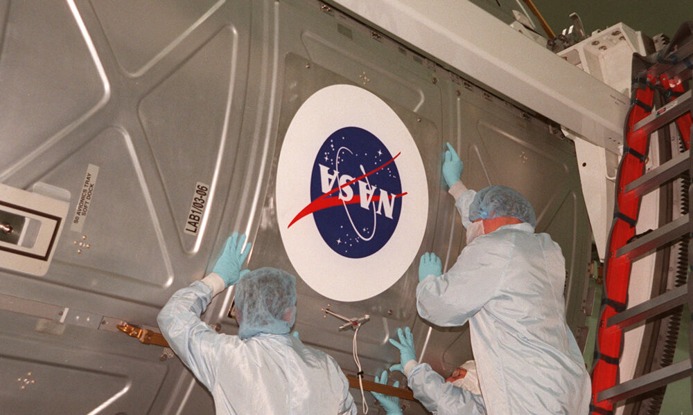 Workers apply a NASA logo to a payload