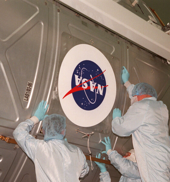 Workers apply a NASA logo to a payload