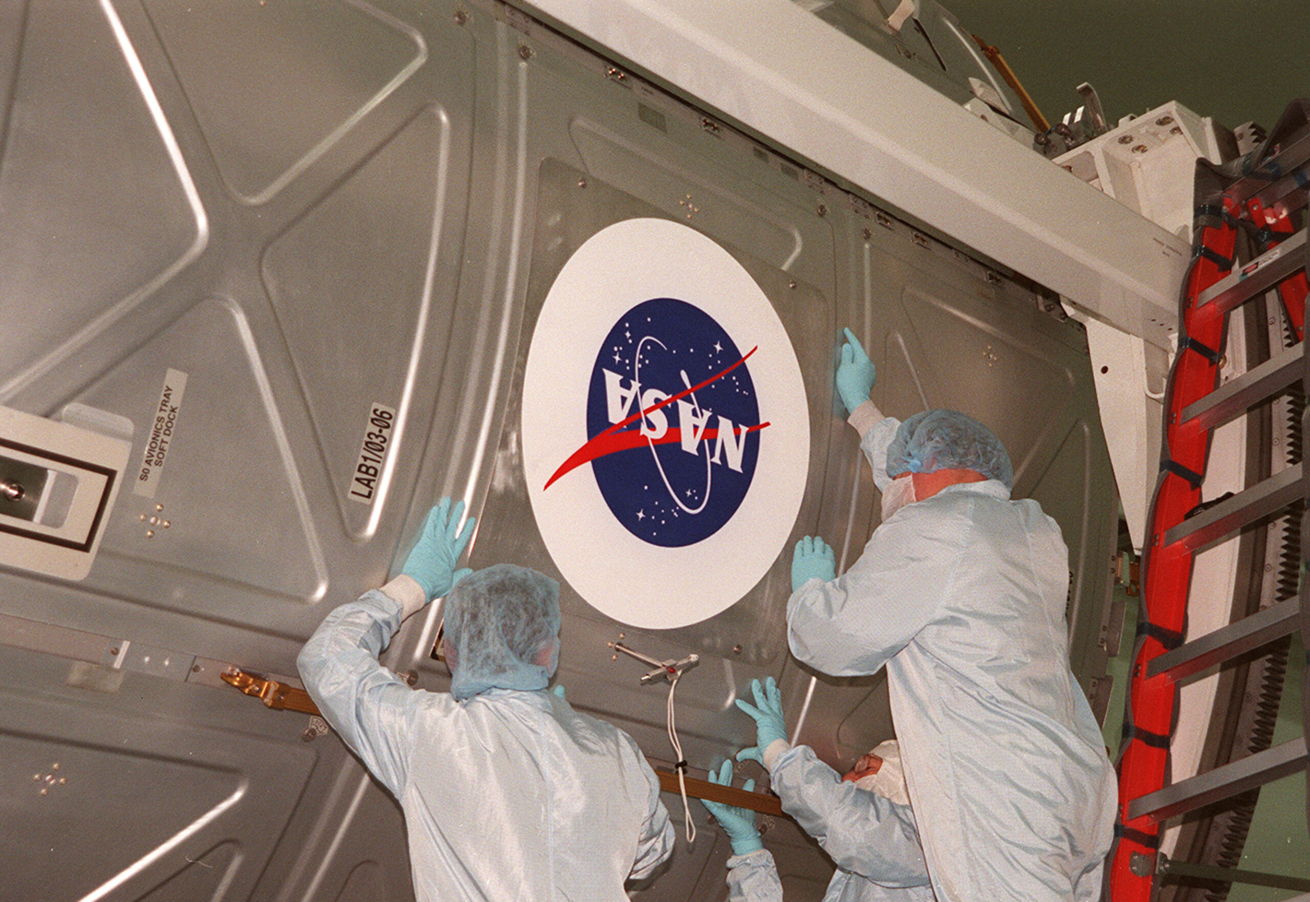 Workers apply a NASA logo to a payload